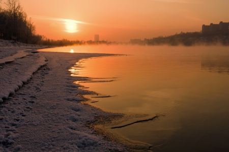 The setting sun illuminating the river, covered with snowの写真素材