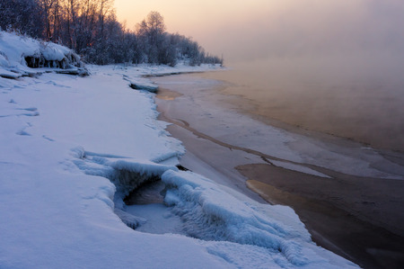 river covered with snow and illuminated with light of the setting sunの写真素材