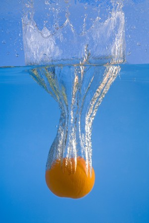 A photo of an orange fruit falling and splashing into waterの写真素材