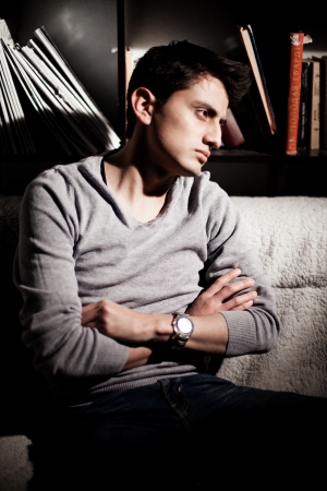 A young brunet man look away and sitting in a dark libraryの写真素材