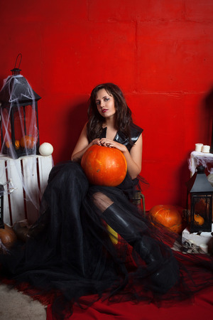 Gothic girl in dress sitting with a pumpkinの写真素材