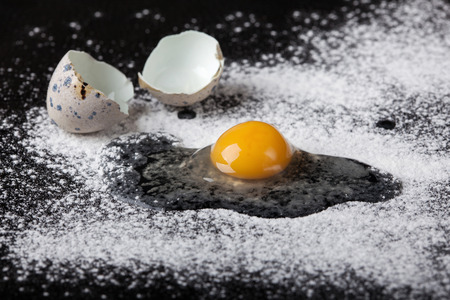 One quail egg broken into flour on black background, soft focusの写真素材
