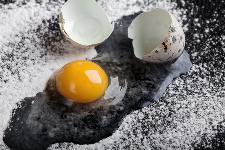 One quail egg broken into flour on black backgroundの写真素材