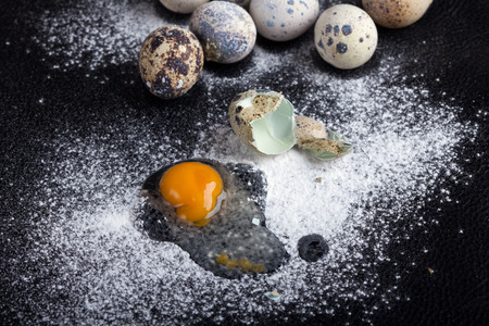 One quail egg broken into flour on black background, soft focusの写真素材