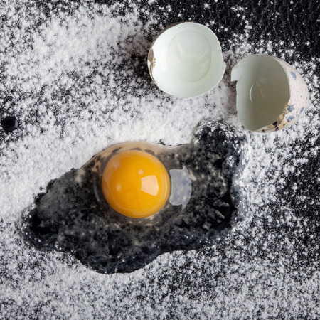One quail egg broken into flour on black backgroundの写真素材