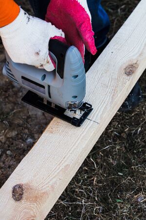 a man in gloves saws an electric jigsaw raw boardの写真素材
