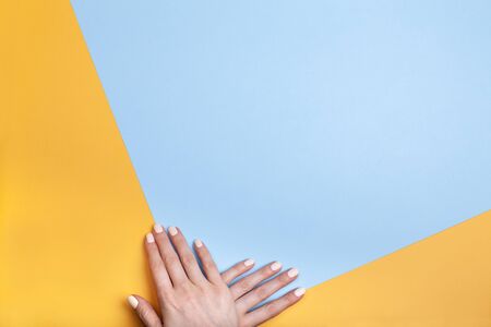 Beautiful female hands with a classic matte manicure on a blue-yellow background. Place for your text.の写真素材
