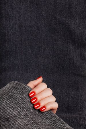 A hand with a red manicure holds a gray denim. Background with place for text.の写真素材