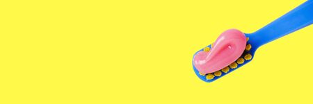 Bright toothbrush with pink paste close-up on a yellow background. Banner format