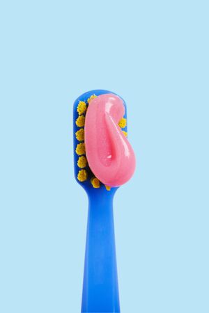 Bright toothbrush with pink paste close-up on a blue background.