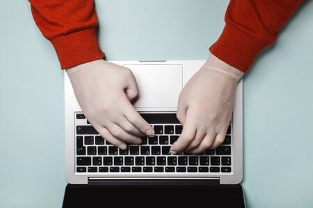 A man works in disposable medical gloves at a laptop.