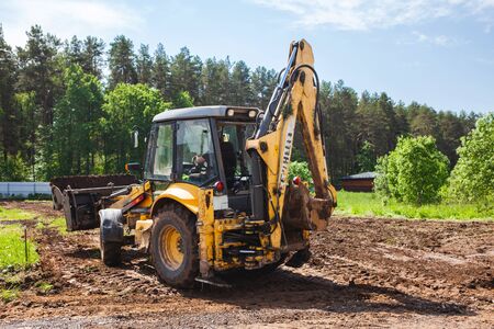 Clearing and leveling a private land plot. Yellow excavator driven earth in a wide bucket, back viewの写真素材