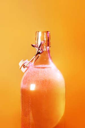 Shining bright chilled glass bottle on an orange background. Summer concept of clean fresh drinking waterの写真素材