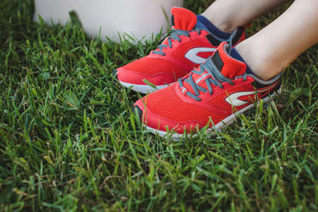 Girl in red sports sneakers sits resting on the grass in the park after jogging. Legs close up
