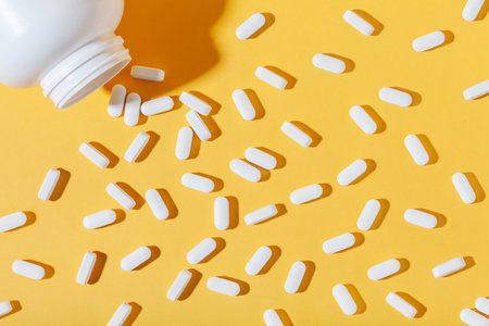 White pills are poured from a jar on a yellow background. Food supplement, multivitamins, medicationsの写真素材