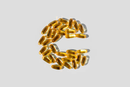 Yellow gelatin capsules on a gray background in the shape of the letter C. Food supplement, vitamin C.の写真素材