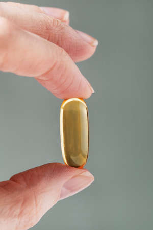 Female hand holding a big yellow capsule of nutritional supplement . Food supplement, vitamin D, omega, vitamin C, multivitaminsの写真素材