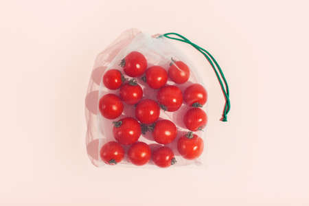 Reusable packaging of products by weight. Red tomatoes in a reusable bag close up on a pink background.の写真素材