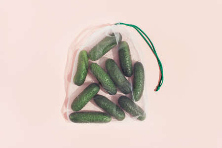 Reusable packaging of products by weight. Cucumbers in a reusable bag close up on a pink backgroundの写真素材