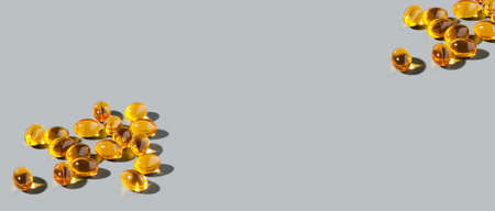 Yellow gelatin capsules on a gray background. Food supplement, vitamin D, omega, vitamin C, multivitamins. Banner with copy spaceの写真素材