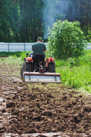 Clearing and leveling a private land plot. A man on a track cultivator digs a private plotの写真素材