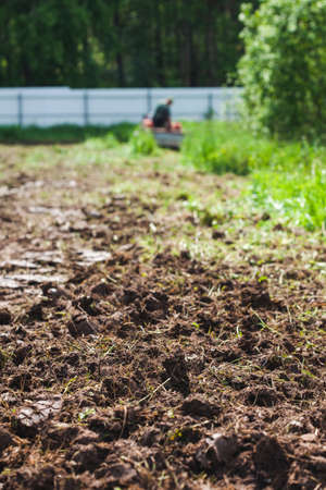 A man on a track cultivator digs a private plot. Focus on the foreground on clods of earthの写真素材
