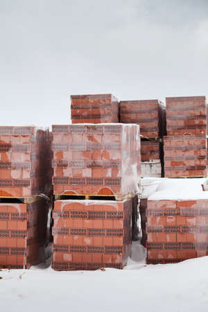 Preparing for the construction of a house, a break from construction for the winter. Packages of red bricks lie outside under the snowの写真素材