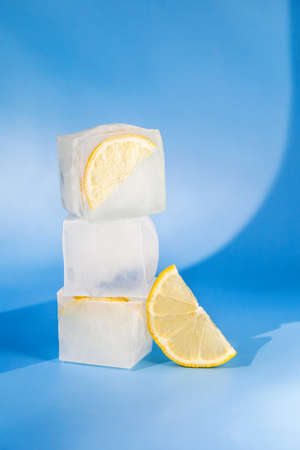 Modern composition of the frozen slices of lemon and ice cubes on a blue background