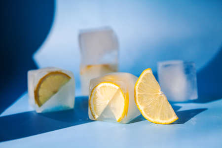 Modern composition of the frozen slices of lemon and ice cubes on a blue backgroundの写真素材