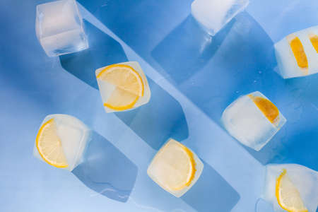 Modern composition of the frozen slices of lemon and ice cubes on a blue backgroundの写真素材