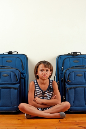 A young girl sits in front of suitcases, with a sad expression on her face.の写真素材