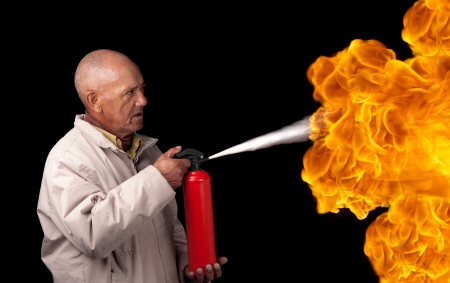 An old man attempts to extinguish the flames of a giant fire with a small extinguisher の写真素材