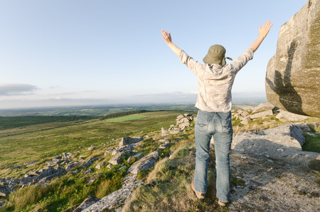 Woman wearing hat with arms outstretched standing on Kilmar Tor a high peak on Bodmin Moor in Cornwallの写真素材