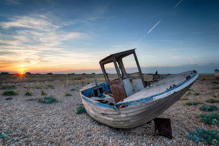 An old abandoned wooden fishing boat with nets washed up on a shingle beachの写真素材
