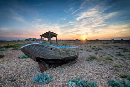 Sunset over an old wooden boat wrecked on a pebble beachの写真素材