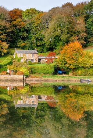 A beautiful cottage surrounded by Autumn colour and reflected in a lakeの写真素材