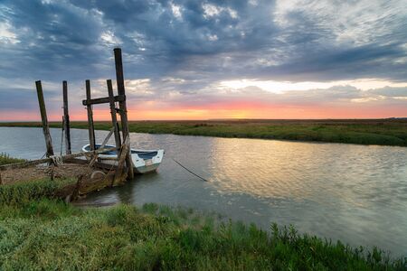 Sunrise over a boat moored to an old wooden jetty at Thornham on the Norfolk coastの写真素材