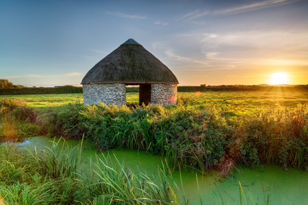 Sunset over a thatched round linhay barn on Braunton Marshes near Barnstaple in Devonの写真素材