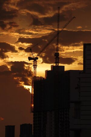 The beautiful golden color of Sunset view with the silhouette of crane not working because of construction project delay during Covid-19 / Coronaの写真素材