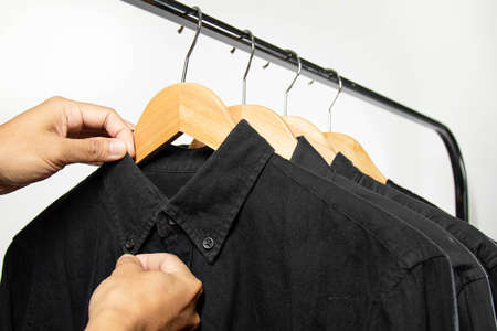 Close-up shot of a young man, fasteners the button of black cotton shirt, on black rack.の写真素材