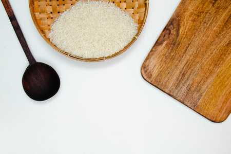 A long grain white rice, on rattan handmade bowl with wooden spoon isolated and black walnut chopping board on white background. Copy spaceの写真素材