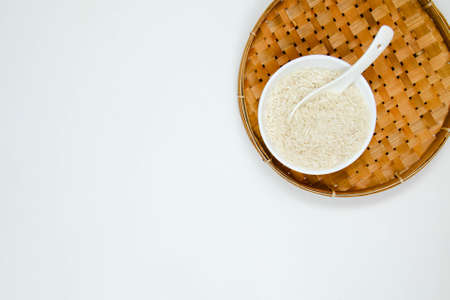 A white ceramic bowl and spoon and of long grain white rice, on rattan handmade bowl isolated on white background. Copy spaceの写真素材