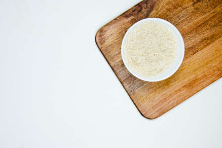 Bowl of long grain white rice, on black walnut chopping board isolated on white background. Copy spaceの写真素材