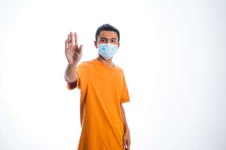 the concept of health care and medicine. A young man standing in a face mask with hand gesture "stop", supporting social distanceの写真素材