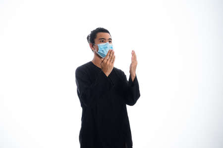 the concept of health care and medicine. A young man pray in a face mask, supporting social distanceの写真素材
