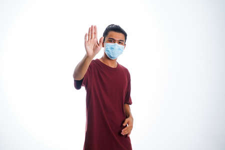 the concept of health care and medicine. A young man standing in a face mask with hand gesture "stop", supporting social distanceの写真素材
