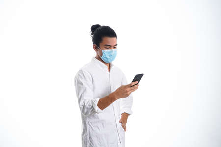 the concept of health care and medicine. A young man reading a news on his phone in a face mask, supporting social distanceの写真素材