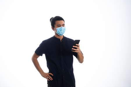 the concept of health care and medicine. A young man reading a news on his phone in a face mask, supporting social distanceの写真素材