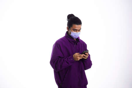 the concept of health care and medicine. A young man reading a news on his phone in a face mask, supporting social distanceの写真素材