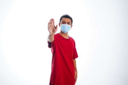 the concept of health care and medicine. A young man standing in a face mask with hand gesture "stop", supporting social distanceの写真素材